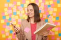 Portrait of smiling joyful delighted brown haired woman wearing beige jacket, using cell phone for checking e-mail, working with Royalty Free Stock Photo