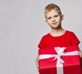 Portrait of smiling kid boy in red t-shirt holding big present box with ribbon in hands, carrying it, ready for birthday Royalty Free Stock Photo