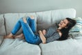 laughing Caucasian young beautiful woman model with messy long hair in ripped blue jeans and striped t-shirt lying on sofa