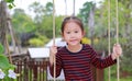 Portrait of smiling little Asian child girl play and sitting on the swing in the nature park Royalty Free Stock Photo