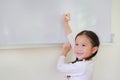 Portrait of Smiling little Asian child girl or Schoolgirl writing something on whiteboard with a marker and looking up in the