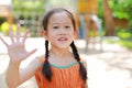 Portrait of smiling little Asian child girl showing palm or high five fingers for stop sign in the garden outdoor. Focus on kid Royalty Free Stock Photo