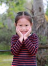 Portrait of smiling little Asian kid girl with touching her cheek looking straight at camera in the nature garden Royalty Free Stock Photo