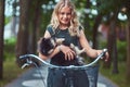 Portrait of a little blonde girl in a casual dress, holds cute spitz dog. Ride on a bicycle in the park. Royalty Free Stock Photo