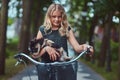 Portrait of a little blonde girl in a casual dress, holds cute spitz dog. Ride on a bicycle in the park. Royalty Free Stock Photo