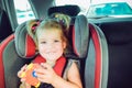 Portrait of smiling little blondy girl looking at camera and sitting in baby car seat. Child fastened with security belt in safety