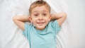 Portrait of smiling little boy in pajamas lying on big bed with white sheets and looking up in the camera. Concept of Royalty Free Stock Photo