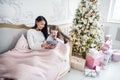 Portrait of smiling little daughter sitting together with her mother and using digital tablet at home at christmas time. Royalty Free Stock Photo