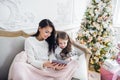 Portrait of smiling little daughter sitting together with her mother and using digital tablet at home at christmas time. Royalty Free Stock Photo