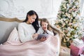 Portrait of smiling little daughter sitting together with her mother and using digital tablet at home at christmas time. Royalty Free Stock Photo