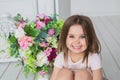 Portrait of a smiling little girl in a light pink dress sits on a floor near a flowers in a studio Royalty Free Stock Photo