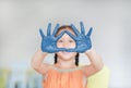 Portrait of smiling little girl looking through her blue hands painted in kids room. Focus at baby hands Royalty Free Stock Photo