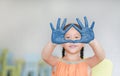 Portrait of smiling little girl looking through her blue hands painted in kids room. Focus at baby hands Royalty Free Stock Photo