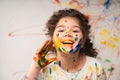 Portrait of smiling little girl looking through her colorful hands and cheek  painted in kids room. Royalty Free Stock Photo