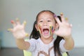 Portrait of smiling little girl looking through her colorful hands and cheek painted in kids room. Focus at baby face Royalty Free Stock Photo