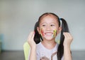 Portrait of smiling little girl looking through her colorful hands and cheek painted in kids room. Focus at baby face Royalty Free Stock Photo