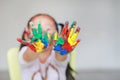 Portrait of smiling little girl looking through her colorful hands and cheek painted in kids room. Focus at baby hands Royalty Free Stock Photo