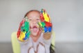 Portrait of smiling little girl looking through her colorful hands and cheek painted in kids room. Focus at baby hands Royalty Free Stock Photo