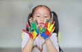 Portrait of smiling little girl looking through her colorful hands and cheek painted in kids room. Focus at baby hands Royalty Free Stock Photo