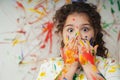 Portrait of smiling little girl looking through her colorful hands and cheek painted in kids room Royalty Free Stock Photo