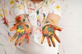 portrait of smiling little girl looking through her colorful hands and cheek painted in kids room. Royalty Free Stock Photo