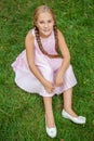 Portrait of a smiling little girl sitting on green grass with toothy smile and pigtail hair style looking at camera and happy. top Royalty Free Stock Photo