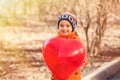 Smiling little toddler child in orange jacket and blue hat holding big red heart-shaped balloon. Valentine`s day concept Royalty Free Stock Photo