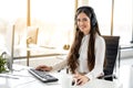 Portrait of smiling long haired woman in headset working on computer and looking at camera in office. Royalty Free Stock Photo