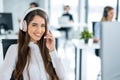 Portrait of smiling long haired woman in headset working on computer and looking at camera in office. Royalty Free Stock Photo