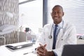 Portrait Of Smiling Male Doctor Wearing White Coat With Stethoscope Sitting Behind Desk In Office Royalty Free Stock Photo