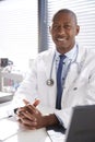 Portrait Of Smiling Male Doctor Wearing White Coat With Stethoscope Sitting Behind Desk In Office Royalty Free Stock Photo
