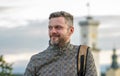 Portrait of a smiling man with a beard of 35-40 years old with a backpack on his shoulder against a blurry background of old archi Royalty Free Stock Photo