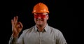 Portrait of a smiling man on a black background in the studio, wearing an construction helmet, protective glasses and a Royalty Free Stock Photo