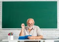 Portrait smiling man in glasses sit at desk. Old man teachers on green board. Happy school male teacher book. Portrait