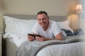 Smiling man lying on bed and using digital tablet in bedroom Royalty Free Stock Photo