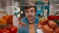 Portrait of a smiling man at the open refrigerator. A man is satisfied with the abundance of food in the refrigerator