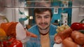 Portrait of a smiling man at the open refrigerator. A man is satisfied with the abundance of food in the refrigerator