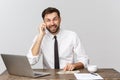 Portrait of smiling man speaking on mobile phone, sitting at desk, looking at computer screen Royalty Free Stock Photo