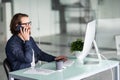 Portrait of smiling business man speaking on mobile phone, sitting at desk, looking at computer screen Royalty Free Stock Photo