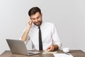 Portrait of smiling man speaking on mobile phone, sitting at desk, looking at computer screen Royalty Free Stock Photo