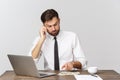 Portrait of smiling man speaking on mobile phone, sitting at desk, looking at computer screen Royalty Free Stock Photo