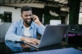 Portrait of smiling african man talking on cell phone while sitting at a cafe with a laptop Royalty Free Stock Photo