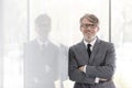 Portrait of smiling mature businessman with arms crossed leaning on wall at office Royalty Free Stock Photo