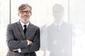 Portrait of smiling mature businessman with arms crossed leaning on wall at office and yellow lens flare in background Royalty Free Stock Photo