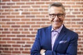 Portrait Of Smiling Mature Businessman Standing Against Brick Wall In Modern Office