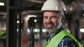 Portrait of Smiling Mature Worker in Safety Vest and Hard Hat. Forklift Driver Looking at Camera. Warehouse with Shelves Royalty Free Stock Photo