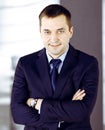 Portrait of a smiling middle aged businessman in a dark blue suit, standing with crossed arms at meeting in an office Royalty Free Stock Photo