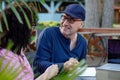 Portrait of smiling middle-aged man sitting at table outdoors, making notes in notebook near laptop, talking with woman. Royalty Free Stock Photo