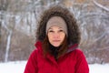 Portrait of smiling middle aged woman with calm look looking at camera in winter park in warm red cloth with hood Royalty Free Stock Photo