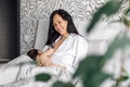 Portrait of smiling mother breastfeeding her infant daughter in bedroom, blurred foreground. Baby suckle milk and get Royalty Free Stock Photo